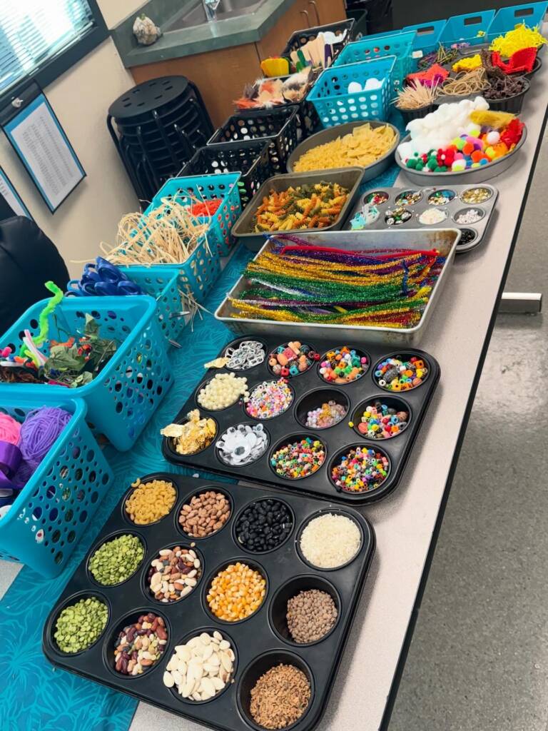 Supplies- Different crafting supplies laid out in small containers or cupcake tins to stay organized. Supplies include beans, rice, beads, can tabs, pipe cleaners, and fabric scraps. 