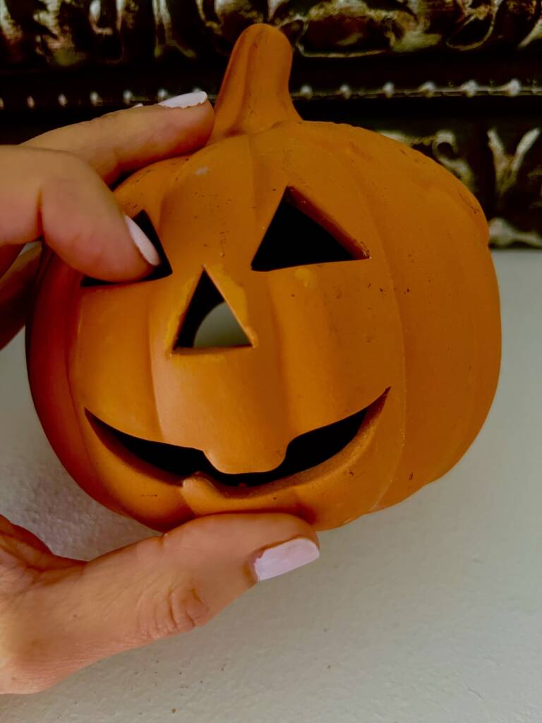 Hand touching a ceramic jack-o-lantern.