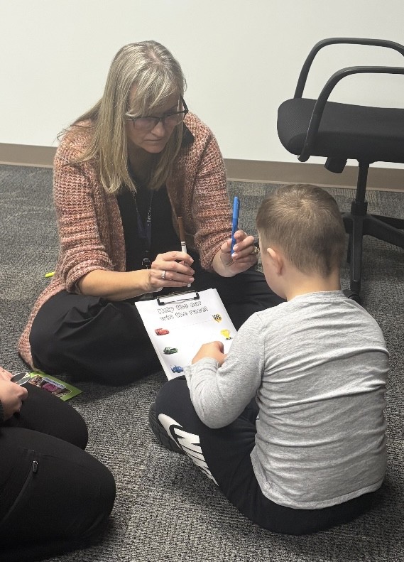 Teacher and student on the floor with a clipboard and worksheet.