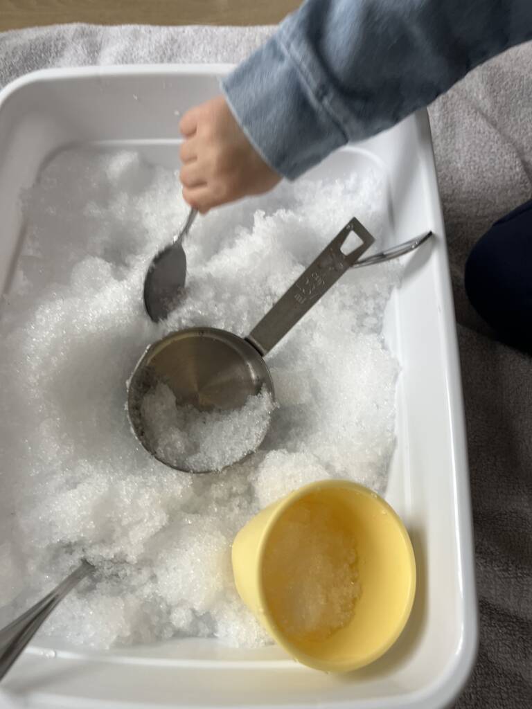 Student scooping snow with a spoon in the container. 