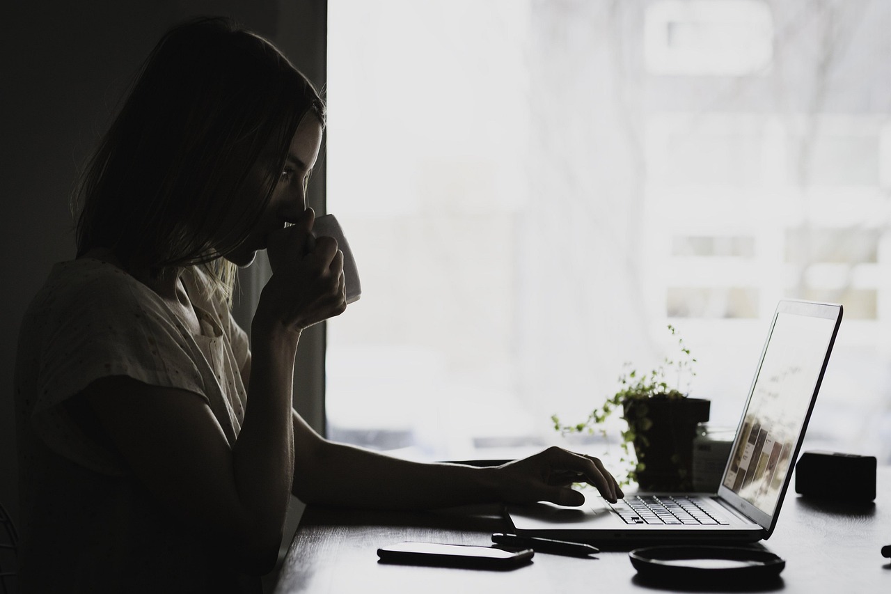 Young woman sitting and looking at her laptop while sipping tea.