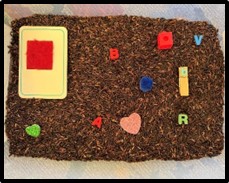 Items in a container with brown rice that include 3D letters and shapes.
