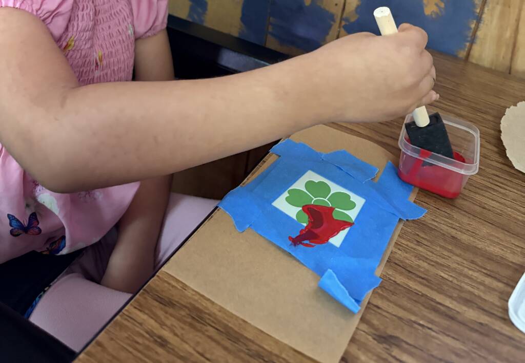 Student dipping foam paint brush in red paint to put on their flower stencil. 