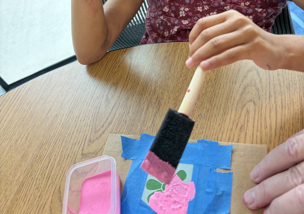 Student painting flower stencil pink.