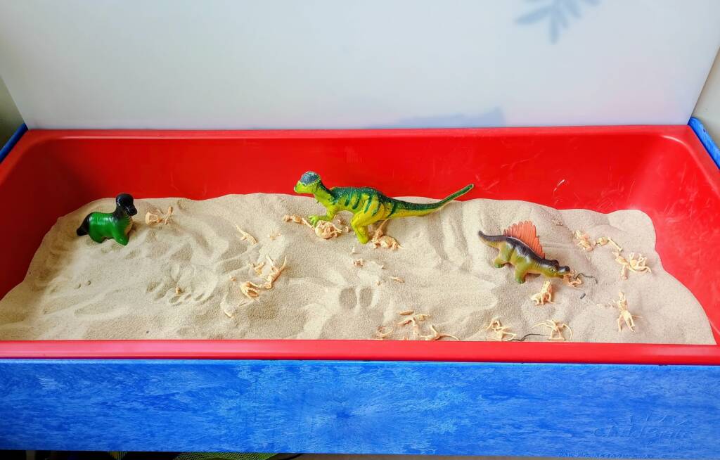 Dinosaur center filled with sand and plastic dinos and fossil bones in the sand.