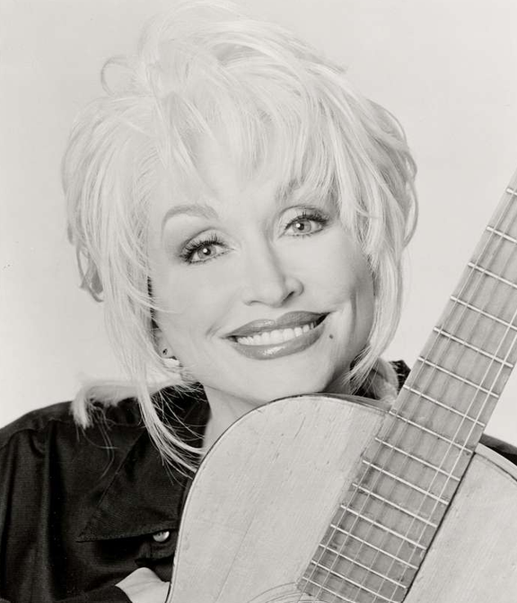 Dolly Parton with a big smile holding her guitar.