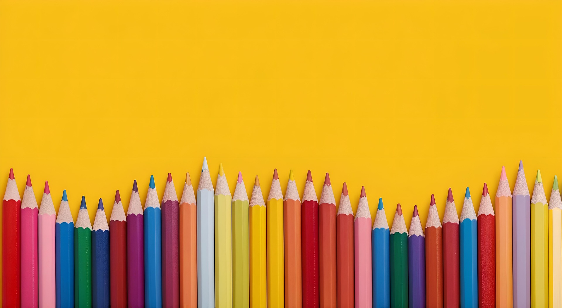 Colored pencils in a row on a yellow backdrop.