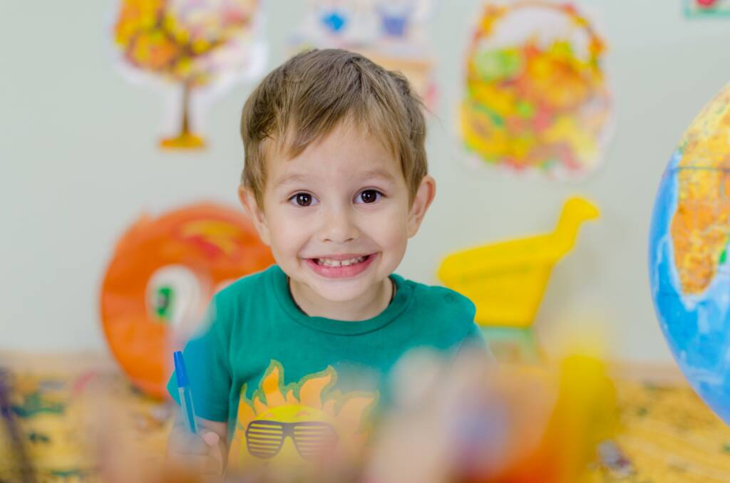 Small boy with a large smile in a colorful classroom setting.