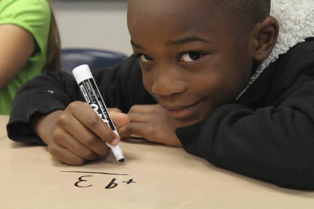 Boy using a whiteboard to do an addition math problem. 