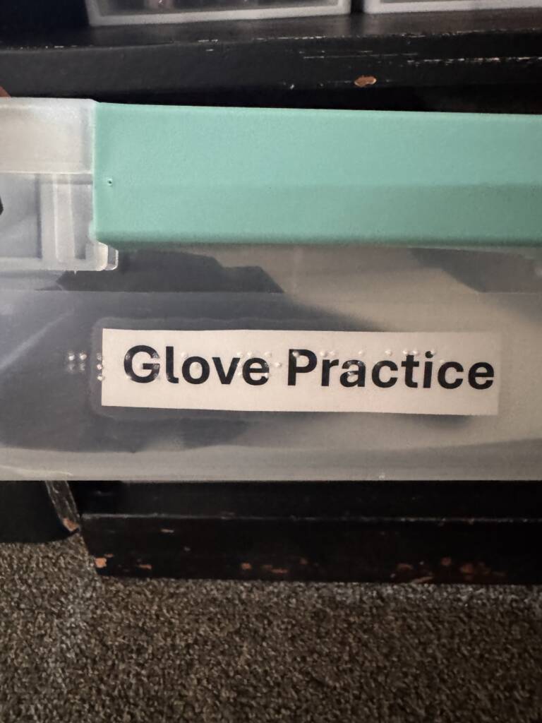 Glove practice box that has large print and braille label on side.