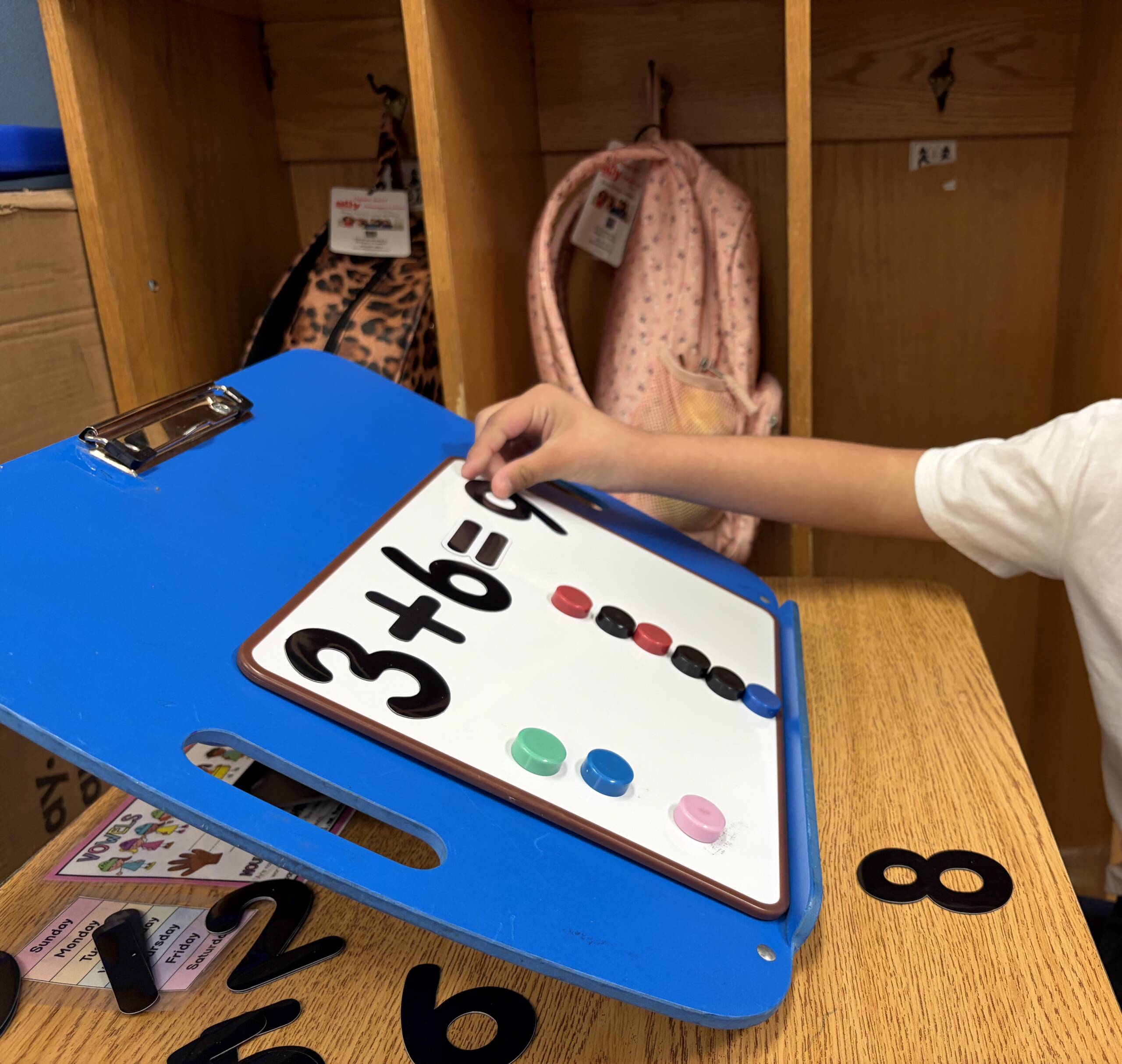 Student at a desk with the slantboard holding the whiteboard. On the board there is an addition problem: 3+6 = 9. There are counter magnets in 2 rows to match the problem.