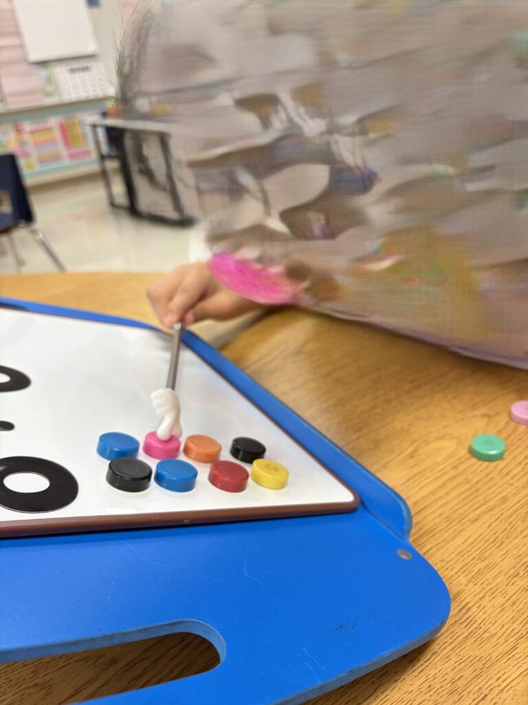 Student using the pointer stick to count the magnets on the whiteboard.  