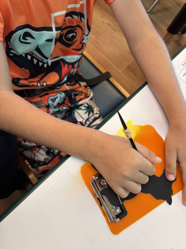 Student using mini clipboard on the table with their scratching tool on the horse craft.